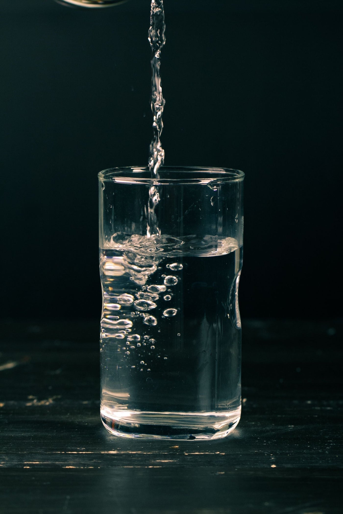 Stream of purified water pouring into a clear drinking glass against a dark background
