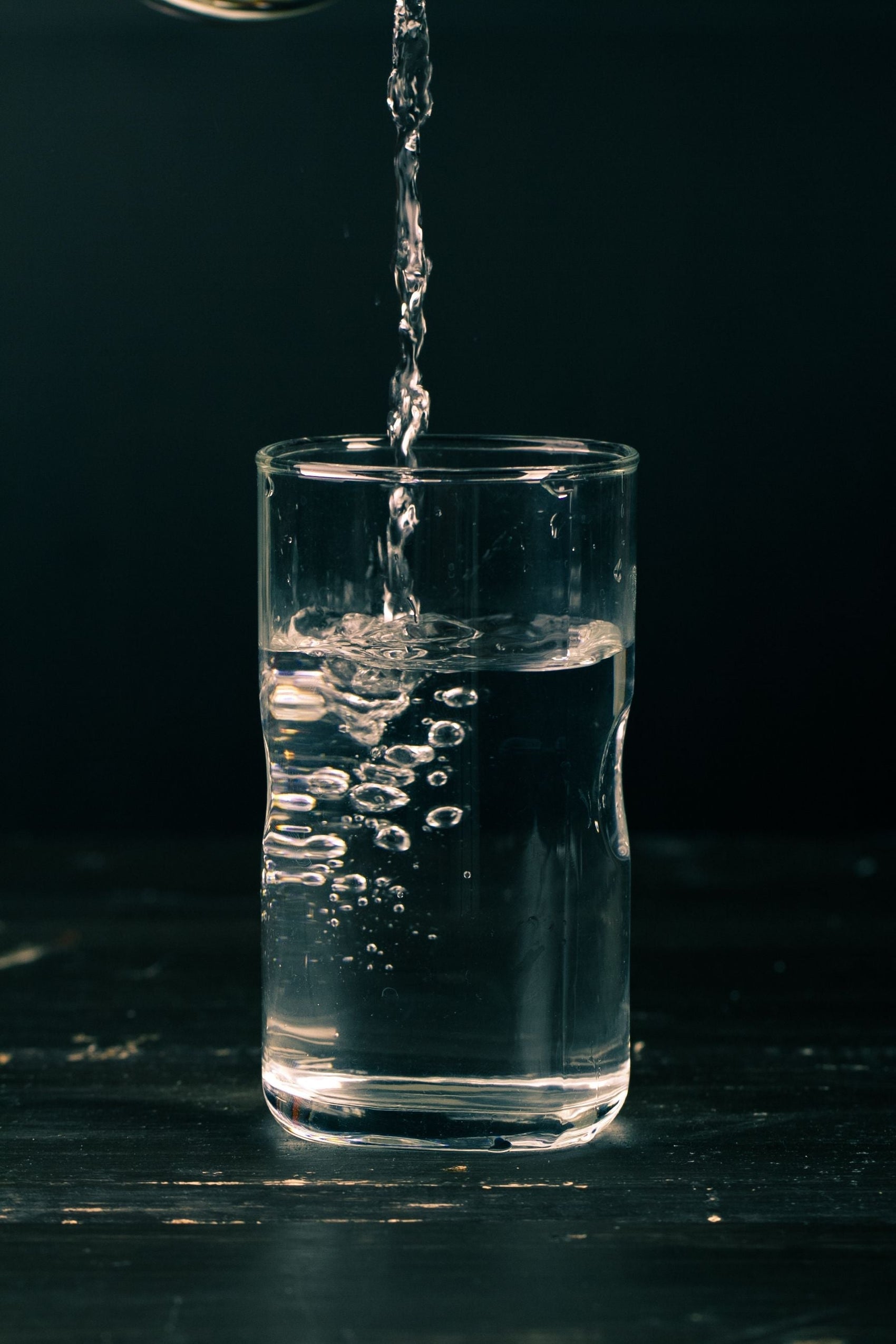 Stream of purified water pouring into a clear drinking glass against a dark background