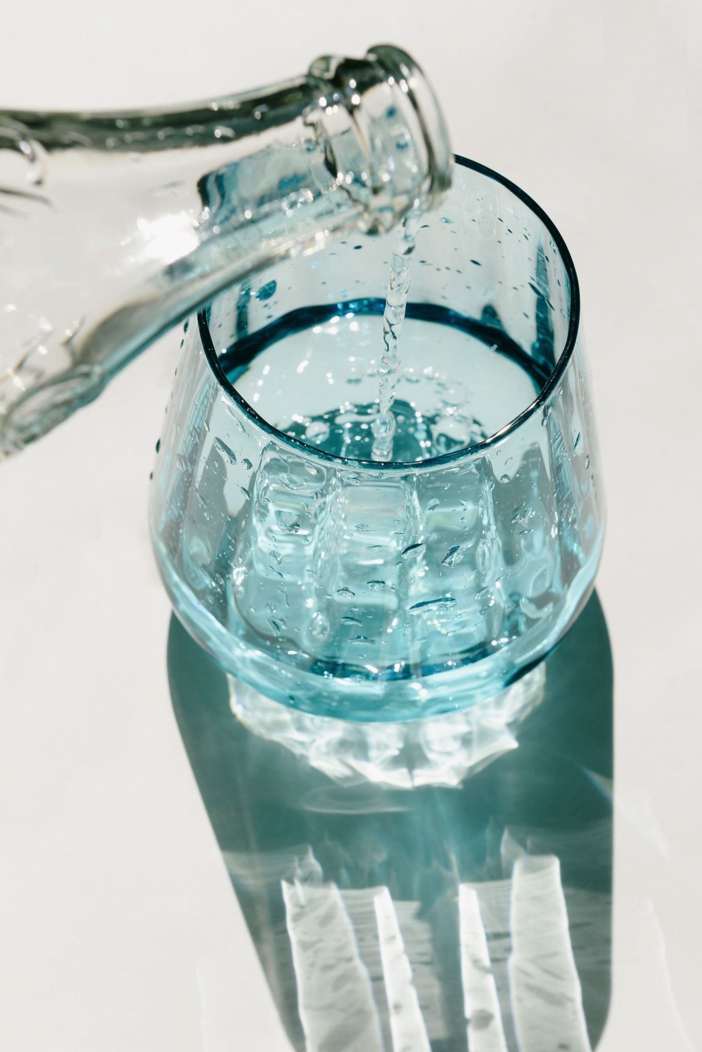 Clean water pouring from a glass bottle into a blue drinking glass in bright light