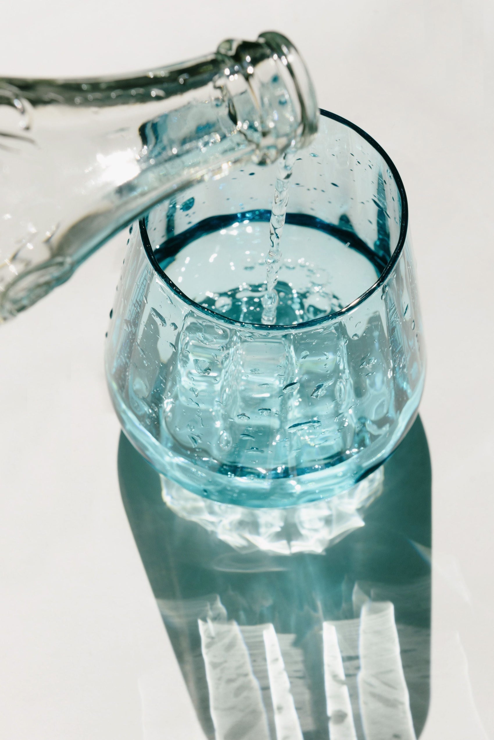 Clean water pouring from a glass bottle into a blue drinking glass in bright light